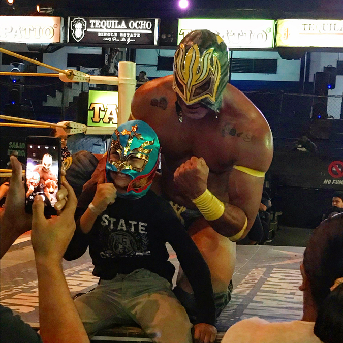 A luchador and young fan posing for pictures at a wrestling match